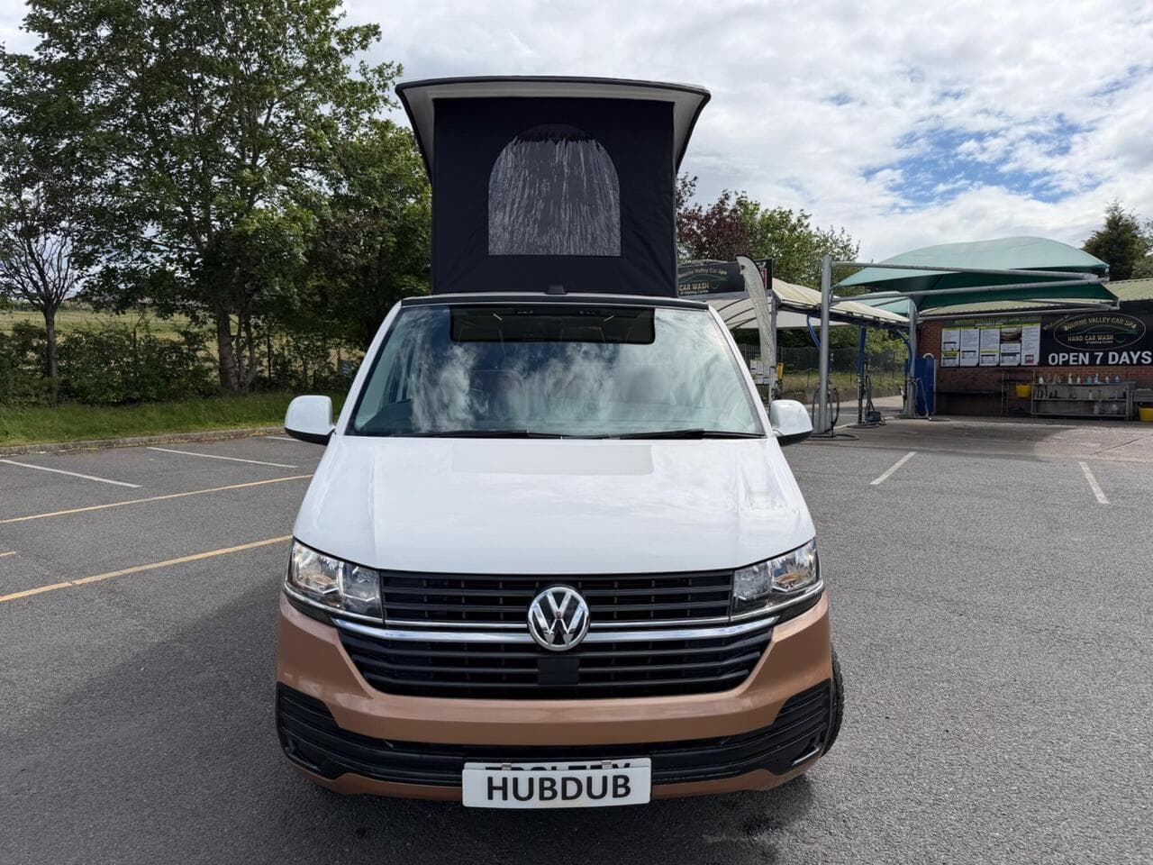 A HubDub-converted VW Transporter in two-tone copper and white with its pop top raised, photographed head-on
