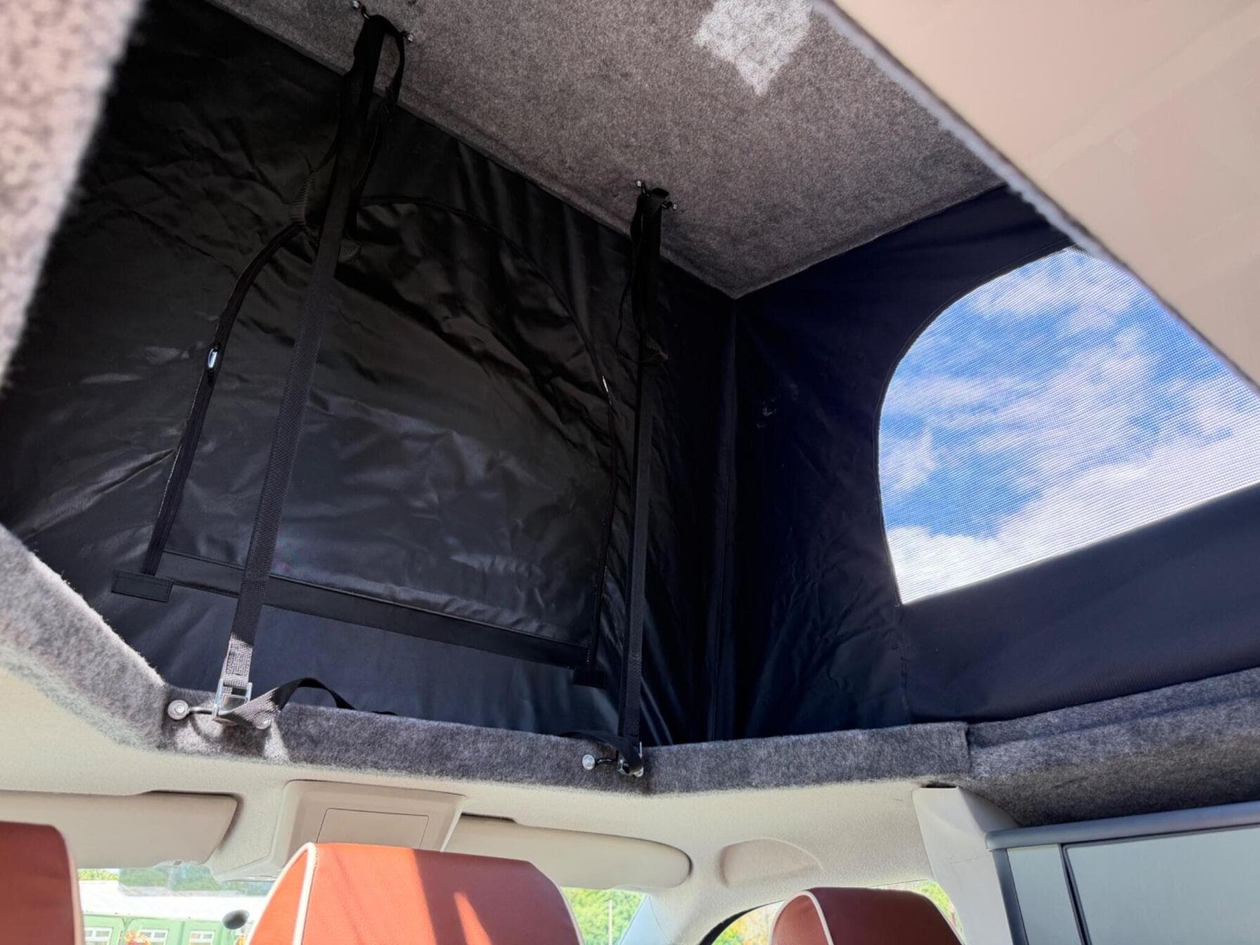 Inside a raised pop-top roof on a HubDub campervan, showing the canvas sides, retaining straps and a mesh ventilation window