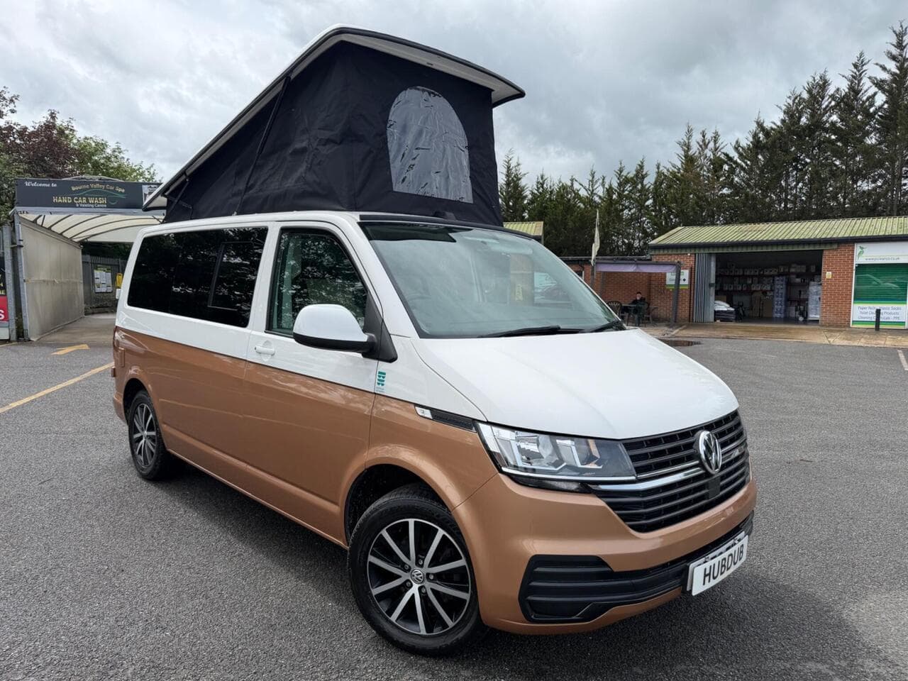 A HubDub-converted VW Transporter T6.1 in two-tone copper and white with its pop top raised, photographed three-quarter front