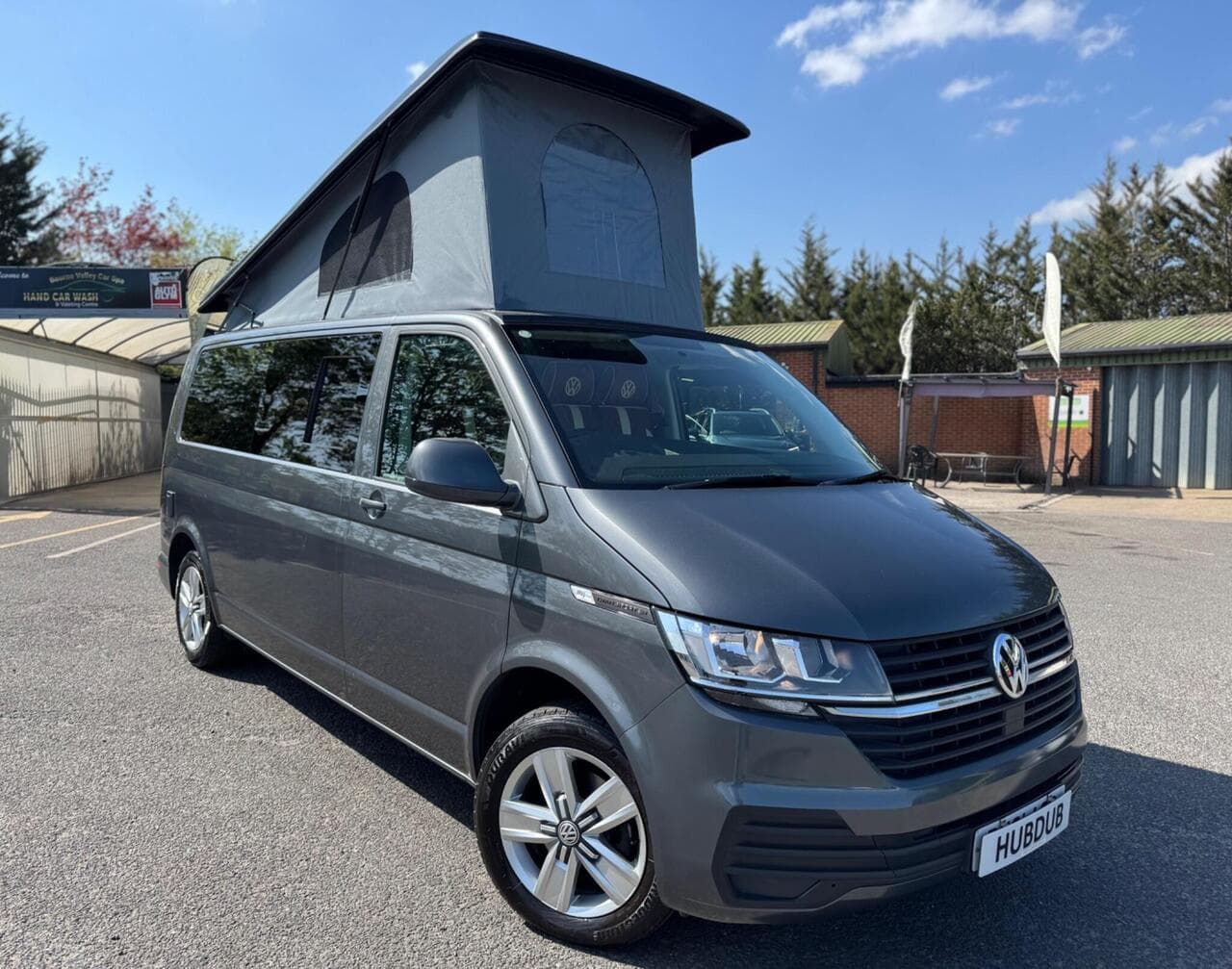 A HubDub-converted VW Transporter with its pop top raised, photographed three-quarter front on the forecourt