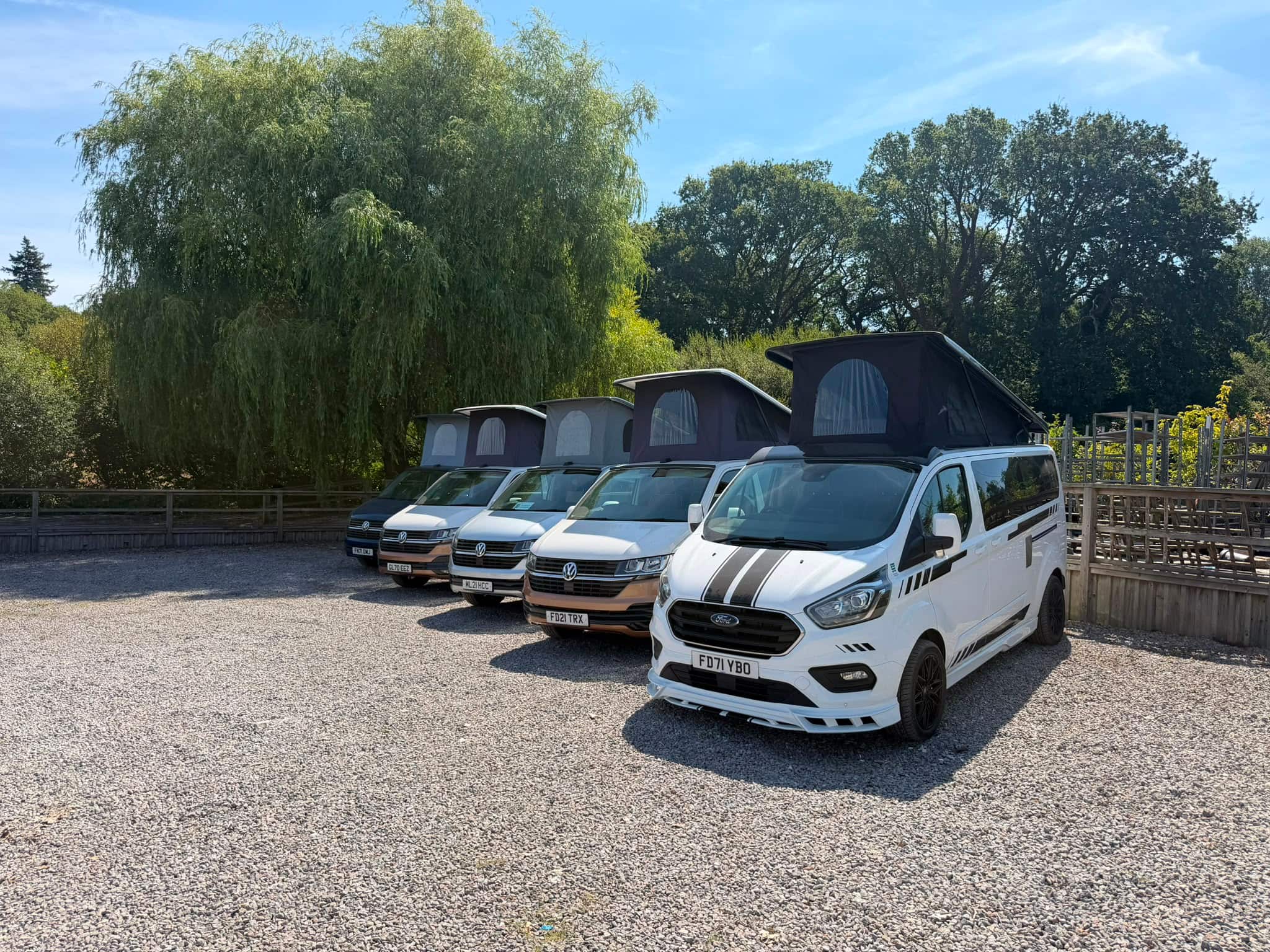 Five HubDub campervans lined up on the gravel at Aylings Garden Centre, Petersfield, four VW Transporters and a Ford Transit Custom with their pop tops raised