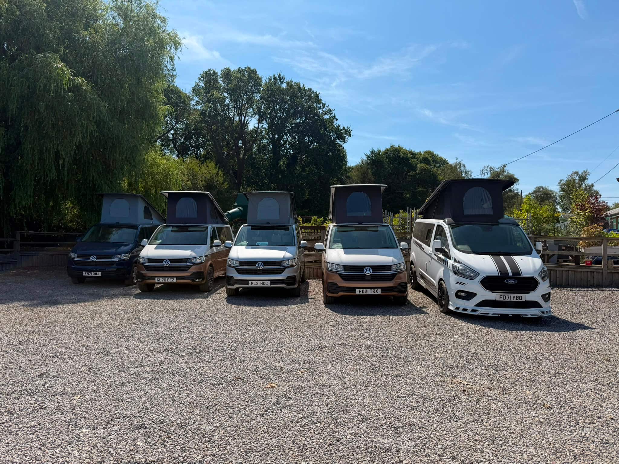 Five HubDub campervans photographed head-on at Aylings Garden Centre, four VW Transporters and a Ford Transit Custom, every pop top raised
